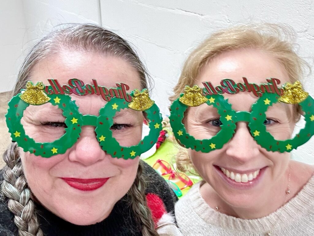 2 female church members smiling with holiday themed novelty glasses on