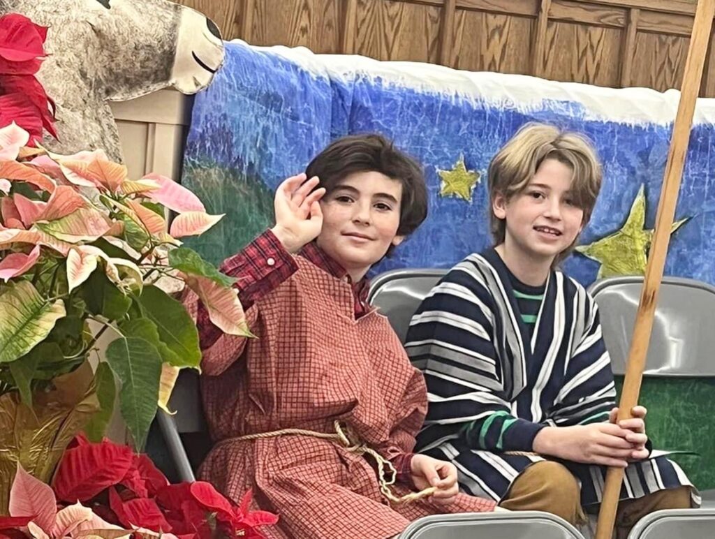2 children smile and wave at camera during christmas pagent